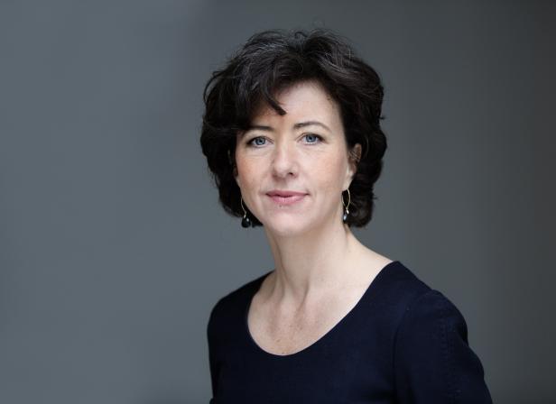 Porträt einer Frau mit dunklen, lockigen Haaren und einem dunklen Oberteil.