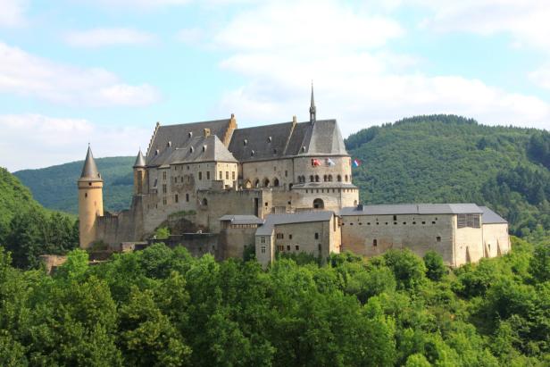 Das Schloss Vianden thront auf einem Hügel, umgeben von grünen Wäldern.