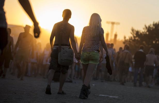 Ein Paar hält Händchen auf einem Festivalgelände im goldenen Abendlicht.