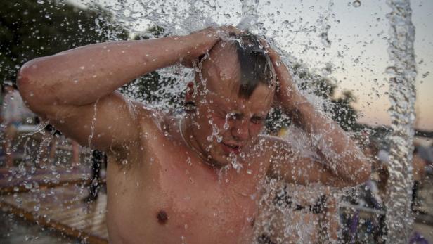 Ein Mann steht unter einer Dusche und hält die Hände über den Kopf.