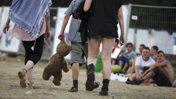 Drei Personen gehen über ein Feld, eine davon trägt einen Teddybären.