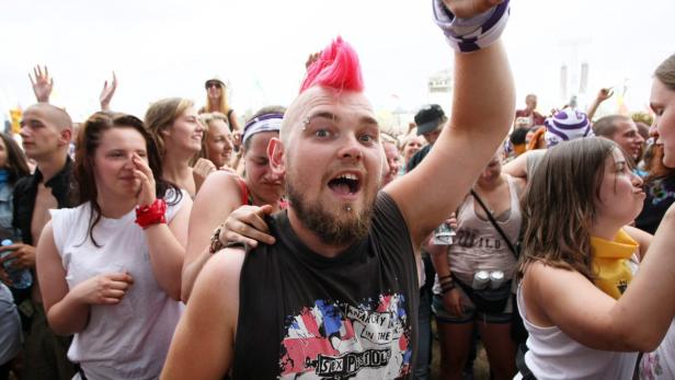 Ein Mann mit pinkem Irokesenschnitt feiert mit anderen Menschen auf einem Festival.