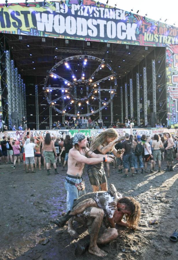 Menschen wälzen sich schlammbedeckt auf dem „Woodstock“-Festival vor einer Bühne.