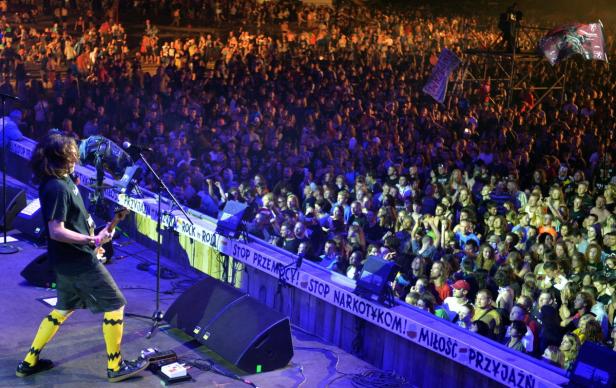 Ein Gitarrist spielt vor einer großen Menschenmenge auf einer Bühne.