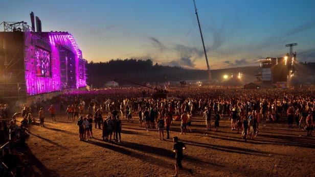 Eine große Menschenmenge versammelt sich vor einer Bühne mit violetter Beleuchtung bei einem Open-Air-Festival.