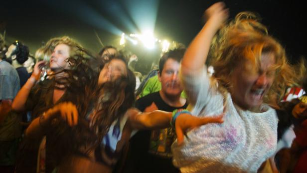 Menschen tanzen und feiern auf einem Konzert vor einer hellen Bühne.