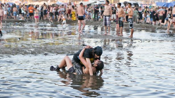 Ein Paar umarmt sich in einem schlammigen Wasserbecken, während im Hintergrund eine Menschenmenge steht.