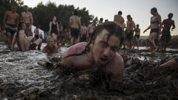Ein Mann liegt schreiend im Schlamm, während andere im Hintergrund stehen.