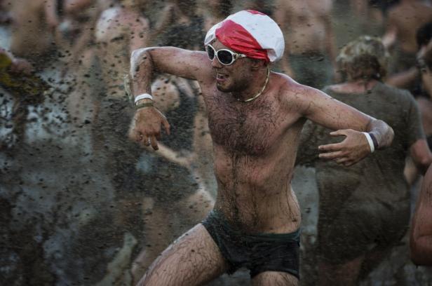 Ein Mann mit Sonnenbrille und Badekappe tanzt schlammbedeckt in der Menge.