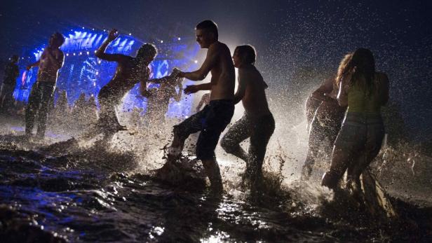 Menschenmenge watet und springt im Schlamm vor einer Bühne.