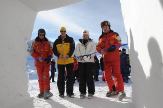Vier Personen durchschneiden ein blaues Band vor einem Tor aus Schnee.