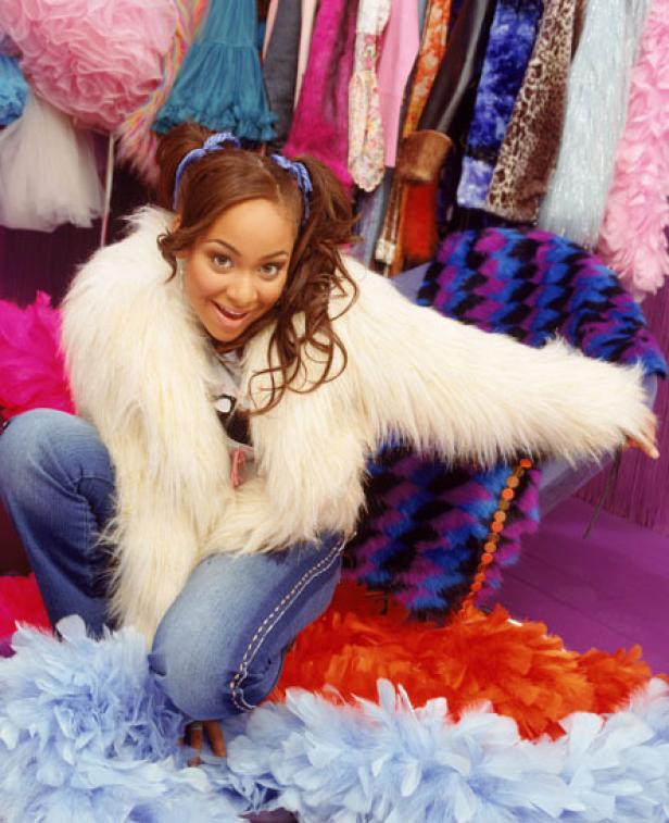 Raven-Symoné posiert in Jeans und einem weißen Fellmantel vor einem Kleiderständer.