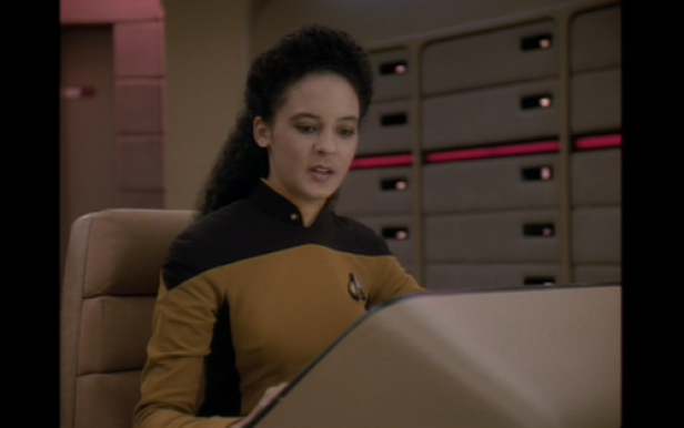 Eine Frau in einer Star Trek-Uniform sitzt an einem Tisch.