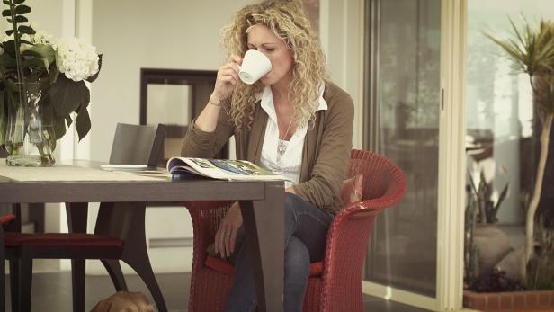Eine Frau mit lockigem Haar trinkt Kaffee und liest eine Zeitschrift.