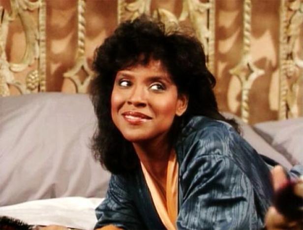 Phylicia Rashad liegt in einem blauen Morgenmantel auf einem Bett.