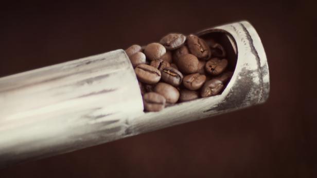 Kaffeebohnen liegen in einem silbernen Röhrchen.