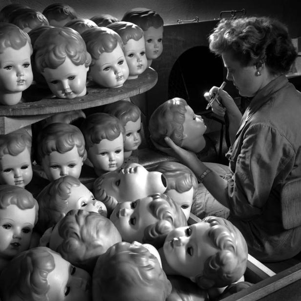 Eine Frau bemalt in einer Fabrik einen Puppenkopf mit einer Spritzpistole.