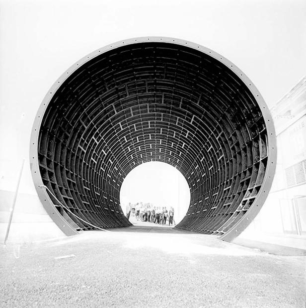 Eine Gruppe von Menschen steht am Ende eines großen, tunnelartigen Rohres.