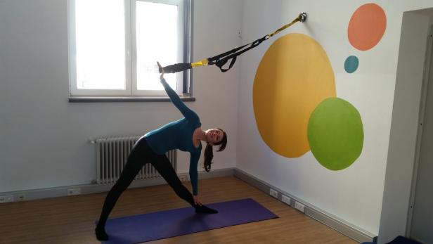 Eine Frau macht Yoga mit einem TRX-Band in einem hellen Raum.