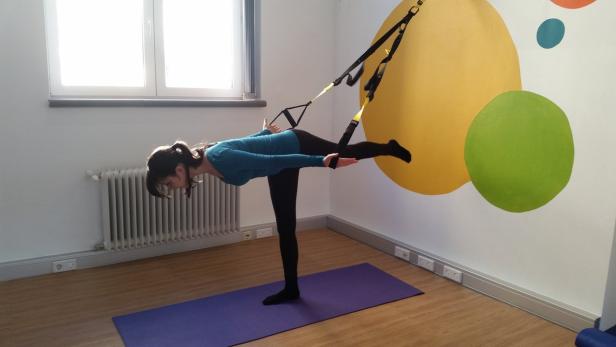 Eine Frau macht mit einem TRX-Band eine Übung für das Gleichgewicht.