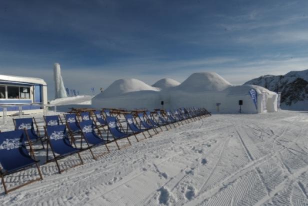 Eine Reihe von Liegestühlen vor einem Iglu-artigen Gebäude im Schnee.