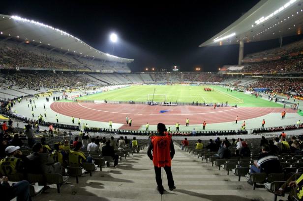 Blick auf ein Fußballstadion mit Laufbahn bei Nacht, gefüllt mit Zuschauern.