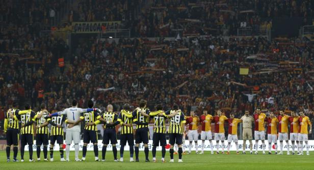 Fußballspieler von Fenerbahçe und Galatasaray stehen vor einem Spiel zusammen auf dem Feld.
