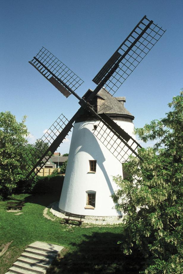 Eine weiße Windmühle mit vier Flügeln unter blauem Himmel.