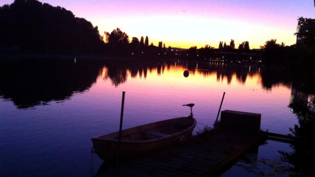 Ein kleines Boot liegt an einem Steg bei Sonnenuntergang an einem See.