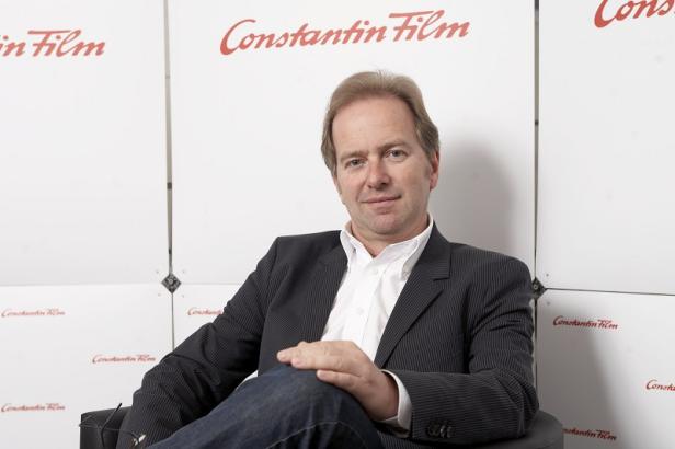 Ein Mann sitzt vor einer Wand mit dem Constantin Film Logo.