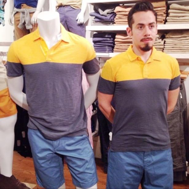 Ein Mann und eine Schaufensterpuppe tragen das gleiche gelb-graue Poloshirt und blaue Shorts.