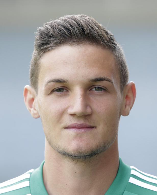 Porträt eines jungen Mannes mit kurzen, braunen Haaren und einem grünen Trikot.