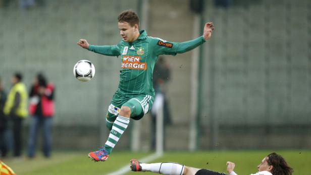 Ein Fußballspieler springt, um einen Ball zu treten, während ein anderer am Boden liegt.