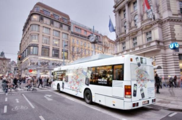 Ein weißer Bus mit Nokia-Werbung fährt durch eine belebte Stadt.