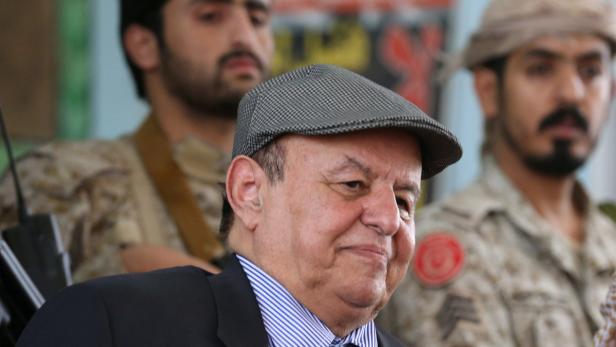 Ein Mann mit Schirmmütze und Anzug vor zwei Soldaten.