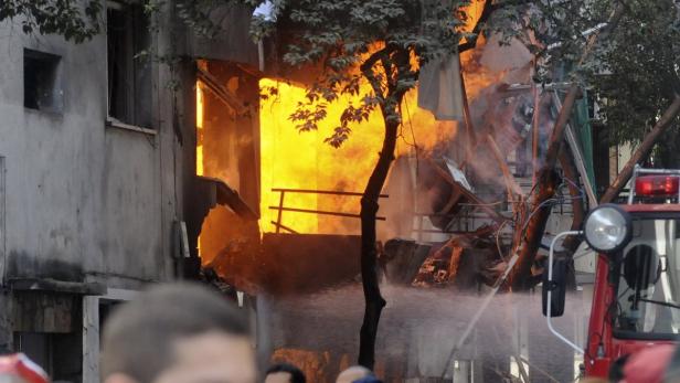 Ein Gebäude steht in Flammen, während ein Feuerwehrauto im Vordergrund Wasser sprüht.