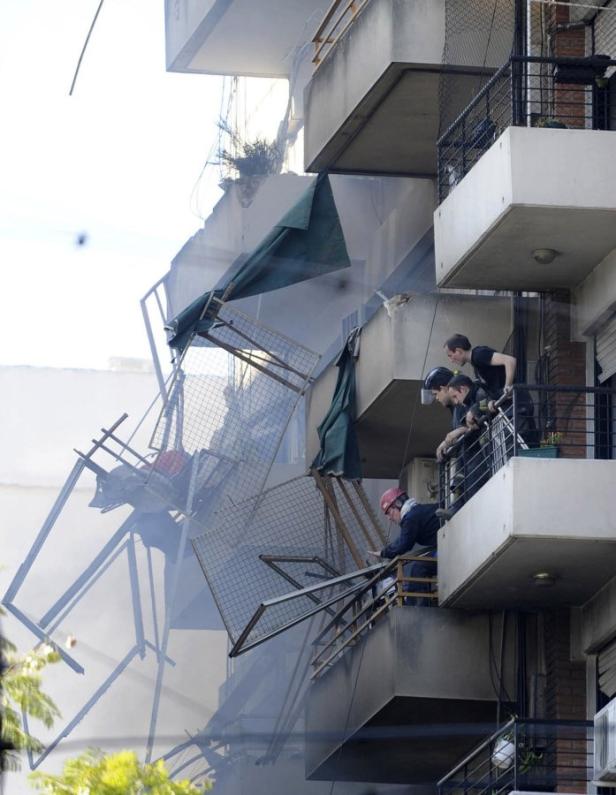 Ein beschädigtes Gebäude mit Trümmern und drei Personen auf einem Balkon.