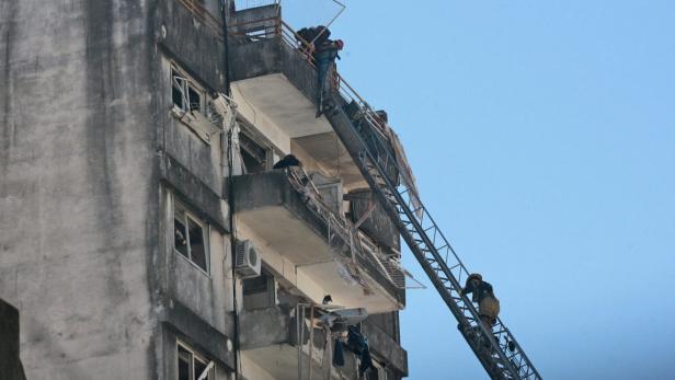 Feuerwehrleute steigen mit einer Leiter zu einem beschädigten Gebäude auf.