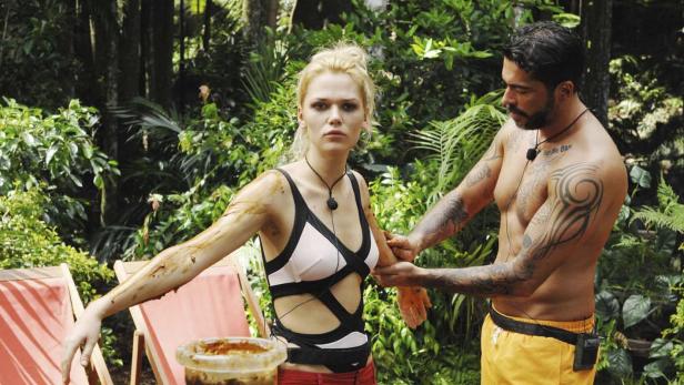 Eine Frau wird im Dschungel von einem Mann mit Schlamm eingerieben.