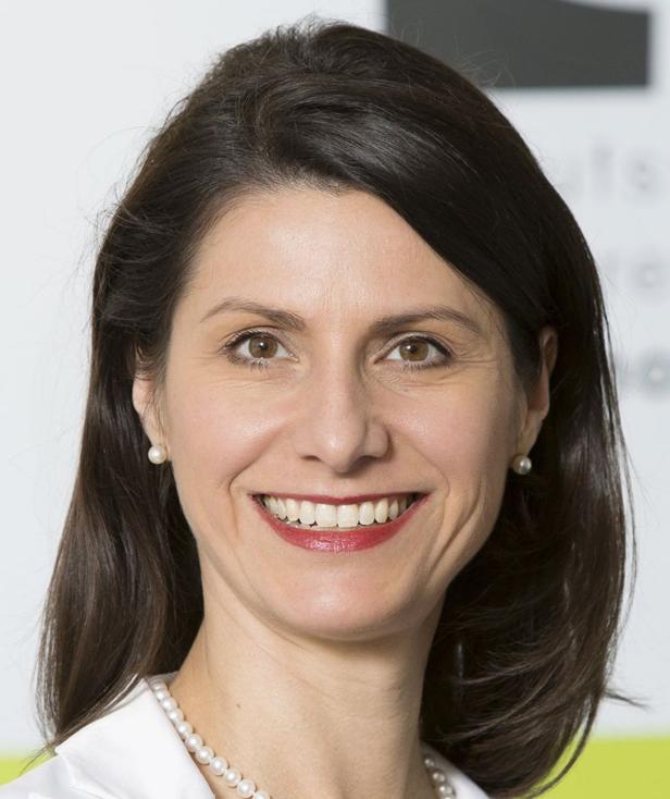 Eine lächelnde Frau mit dunklen Haaren, Perlenohrringen und einer Perlenkette.