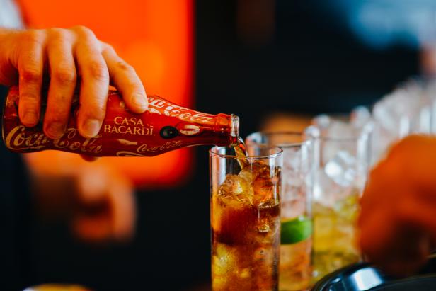 Eine Person gießt Coca-Cola aus einer Flasche in ein Glas mit Eiswürfeln.