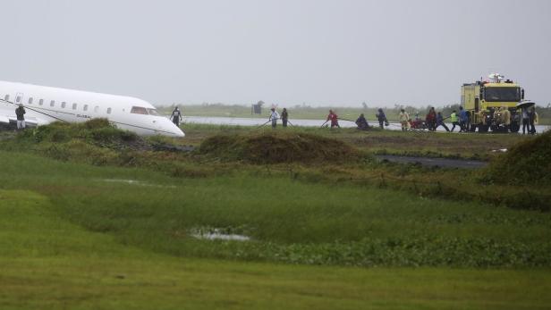 Ein Flugzeug ist neben einer Landebahn im Gras gelandet und wird von mehreren Personen gezogen.