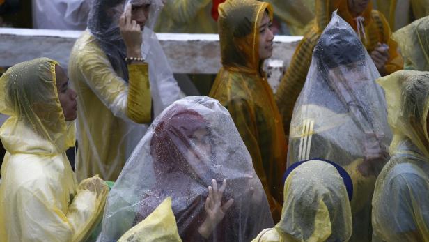Eine Gruppe von Menschen trägt Regenmäntel und transparente Plastikplanen zum Schutz vor dem Regen.