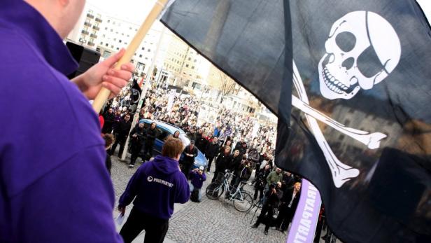 Eine Demonstration mit einer Piratenflagge und Menschenmenge im Hintergrund.