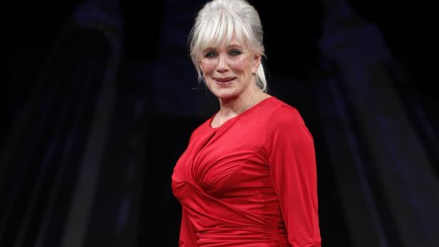 Eine Frau mit weißen Haaren und einem roten Kleid lächelt in die Kamera.