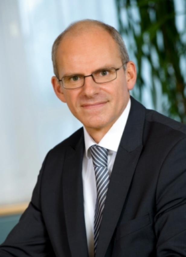 Ein Mann mit Brille, Anzug und Krawatte blickt in die Kamera.