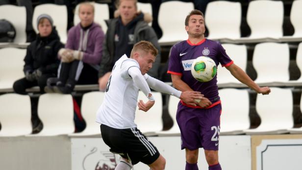 Zwei Fußballspieler kämpfen um den Ball vor einer Zuschauertribüne.