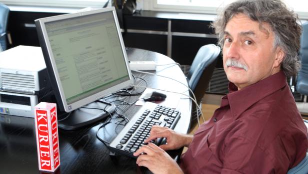 Ein Mann mit Schnurrbart sitzt vor einem Computer und tippt auf der Tastatur.