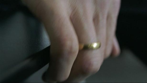 Die Hand einer Person mit einem goldenen Ehering am Finger.