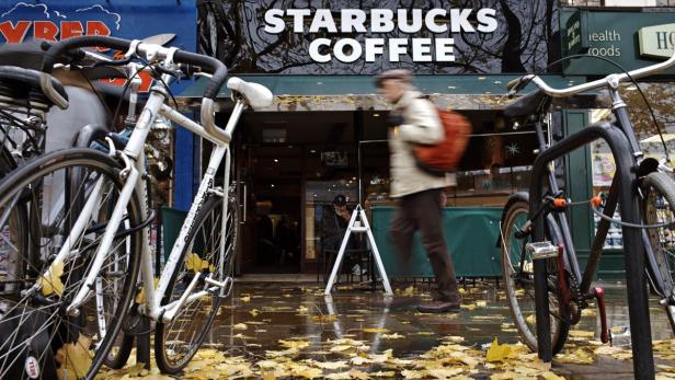 Ein Mann geht an einem regnerischen Tag vor einem Starbucks-Café vorbei, Fahrräder stehen davor.